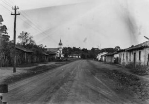 Hauptstraße von Campo Largo : Die Haupstraße des Ortes Campo Largo bei Sorocaba. Rechts Häuser, links ein Mast mit Leitungen. Im Hintergrund eine Kirche.