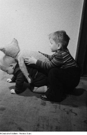 Zwei Kinder spielen mit einem Teddybären