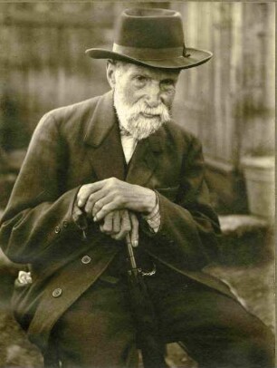Pfälzer Bauer mit weißem Bart. Portrait, sitzend mit Hut, auf Gehstock oder Schirm gestützt