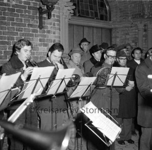 Kirchberg: Weihnachtskonzert vor der Kirche: Posaunenchor der Evangelischen Kirchengemeinde: rechts dahinter vor Kirchenportal Bürgerworthalter Georg Koch und Mitglieder des Oldesloer Männerchores von 1844: Abend: 23.12.1974