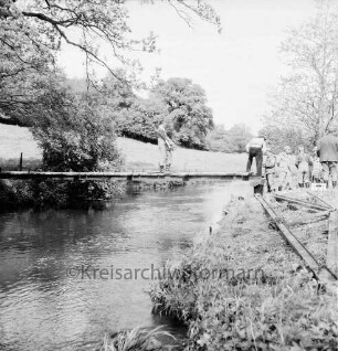 Sühlen: Trave: Wanderweg zwischen Sühlen und Bebensee (Kreis Segeberg): Fußgängerbrücke: Bau: Technisches Hilfswerk (THW) Bad Segeberg: in der Mitte Helfer auf Steg: rechts Gruppe von Helfern an Land beim Verlegen der letzten Holzbohlen: vorn rechts alte Brückenteile: hinten Bäume, Wiese und Wald