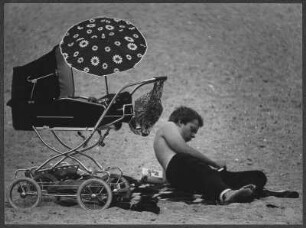 Lesender Mann neben einem Kinderwagen am Strand von Travemünde
