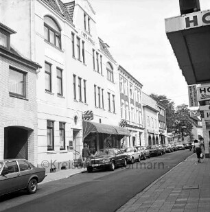 Bahnhofstraße: parkende Pkw und Passanten, rechts das Café Arnold und weitere Wohn- und Geschäftsgebäude