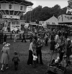 Frühjahrsmarkt: Volksfest: Exer: links Kinder auf Kettenkarussell: vorn und hinten rechts Kinderkarussells mit Kleinkindern: dazwischen Besucher: hinten links Jahrmarktsbuden: hinten Mitte Bäume