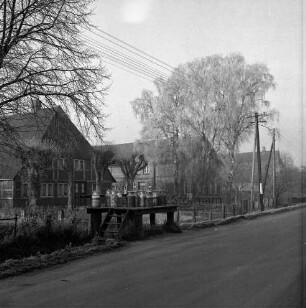 Landwirtschaft: Milchbock mit Milchkannen an Dorfstraße vor Graben: dahinter Bauernhäuser und Bäume