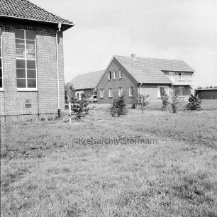 Evangelisch-lutherische Kirchengemeinde Harksheide: "Kirchliches Zentrum am Falkenberg": Kirchenplatz: Blick von Süden: links Falkenberg-Kirche: rechts Pastorat: in der Mitte dahinter der Gemeindesaal: vorn Grünfläche mit Sträuchern