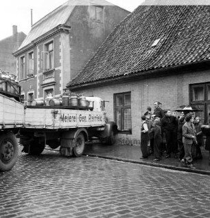 Verkehrsunfall: Lübecker Straße: Lkw fährt in Haus: Unfall-Lkw der Meierei-Genossenschaft Reinfeld mit Anhänger, darauf Milchkannen, mit Kühlerschnauze in Fassade von Eckhaus zu Lübecker Torbrücke: rechts auf Bürgersteig Erwachsene und Kinder als Schaulustige, mit Regenschirm: Straße mit nassem Kopfsteinpflaster