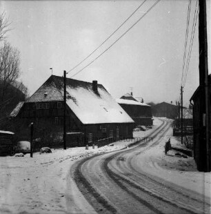 Dorfstraße: rechts und links Strommasten: dahinter Bauernhäuser und Bäume: Winter