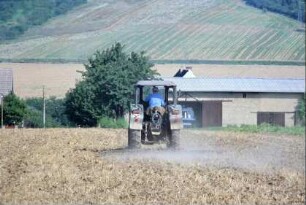 ein alter Traktor auf dem Feld; hinter der Scheune läuft die Ilm