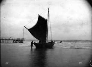 Ostseeküste. Fischerboot am Strand mit gehißtem Segel, daneben Landungssteg