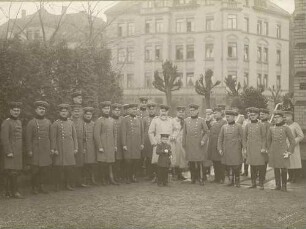 König Wilhelm II. von Württemberg beim Besuch eines Feldartillerie-Regiments in Cannstatt, Garnison Stuttgart mit Offizieren und einem Kind, alle in Uniform und Mütze in einem Hof stehend, Brustbilder meist in Halbprofil