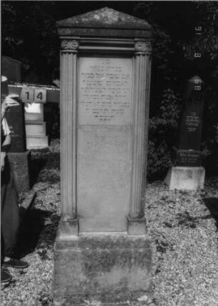Grabstein 14 (Index: 100086628) Material: Sandstein Zustand: leicht verwittert Maße HxBxT: 209x67x36 cm Beschreibung: ädikulaartige Stele mit gerillten Halbsäulen, getreppter Sockel, Giebel: Grabstein 14