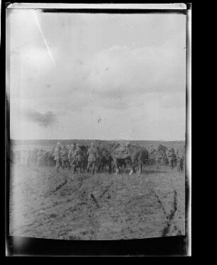 Unbekannte Gegend [Nordfrankreich?]: Soldaten und Offiziere mit Pickelhaube auf einem Feld neben Pferden und Gespannen, im Hintergrund ein langgestreckter Waldrand (Distanzaufnahme)