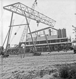 Hartsteinwerk: Rohbau: links Kranwagen mit Ausleger: daran Brückenteil einer Laufkatze: vorn links und hinten Mitte Ständer: hinten Werkhalle im Aufbau
