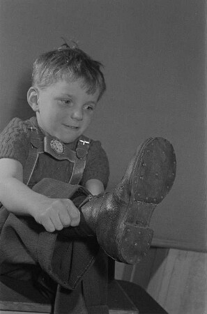Ein Junge (Lothar) zieht sich einen Stiefel an