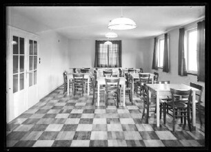 Speisesaal (?) mit hellen Tischen und dunklen Holzstühlen (Jugendherberge?)