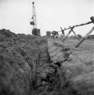 Industriestraße: Absackung eines Teilstücks: in der Mitte Grube: rechts Absperrung, links Erdhaufen: dahinter Bagger, Baubude und Pkw