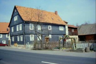 Bauernhaus mit Nebengebäuden an der Hauptstraße; geschmückter Brunnen