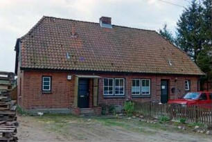 Blumendorf 3: traufständige Doppelkate aus Backstein: Straßenfront: Eingangstüren, Hausnummer, Sprossenfenster: vorne Vorplatz, Zaun, Auto: im Vordergrund links Holzpaletten: 29. April 2003