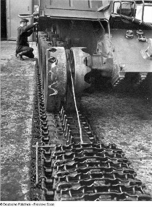 Goldberg (Kreis Lübz). Nationale Volksarmee - Landstreitkräfte. Panzerregiment 8 (PR-8). Freifläche vor Panzerhallen. Soldat bei Instandsetzungs- bzw. Wartungsarbeiten an Gleisketten für Kampfpanzer T-54