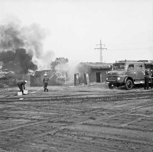 Stemwarde: Kreisfeuerwehrverbandstag: Löschübung: hinten links zwei Feuerwehrmänner beim Löschen von Tankstelle und Wohnhaus: hinten rechts Löschwagen: davor Feuerwehrmann