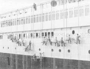14 Männer säubern die Wand eines großen Schiffes