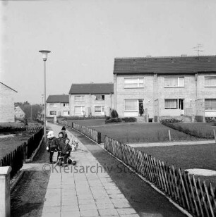 Siedlung Gartenstadt: Schwanenstieg: Reiheneigenheime: Gärten, Jägerzäune: Bildmitte Fußweg, Straßenlampen: spielende Kleinkinder, Dreirad