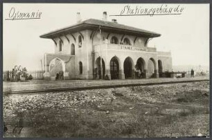 Bahnhof von Osmanyie, Ansicht eines zweistöckigen Gebäudes aus Stein im osmanischen Baustil, mit frei stehendem Torbogen, davor Schienen, einige Personen am Gleis beschäftigt