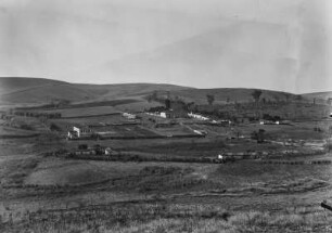 Landschaftsblick : Blick in eine hügelige Landschaft. In der Bildmitte ein ummauertees Grundstück mit einigen Gebäuden.