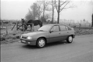 Vorstellung des Opel Kadett GSi 16 V: Seitensicht: auf Straße: dahinter Pferde auf Weide, Zäune, Bäume