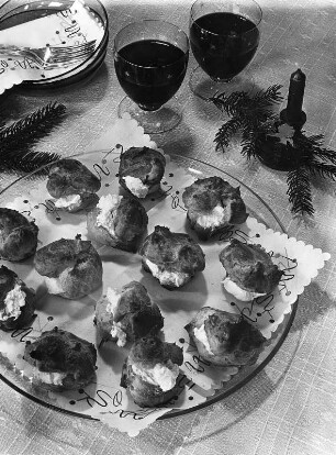 Krafts Rezeptaufnahmen. Glasteller mit gefüllten Windbeuteln. Daneben zwei Gläser mit Rotwein und Kerzenständer mit Tannenzweig