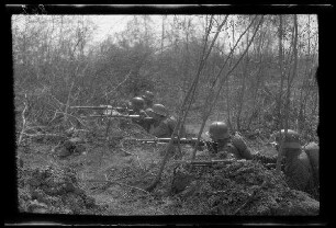 Übungsgelände I bei Mouzon (Dep. Ardennes, Frankreich): 5 Soldaten mit Stahlhelm und aufgelegten Gewehren in einem Graben innerhalb von Buschland (Seitansicht, Nahaufnahme) ("Infanterie im Graben in einem Wald")