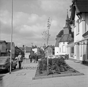 Paul-von-Schoenaich-Straße: Fußgängerweg mit Blumenrabatten: Passanten, Straßenlampen, Verkehrsschilder, parkende Autos: Matthias-Claudius-Kirche: im Hintergrund Bildmitte Rathausturm