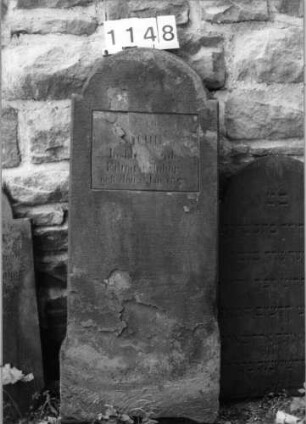 Grabstein 1148 (Index: 99630651) Material: Sandstein Zustand: abgeblättert mit Textverlust Maße HxBxT: 115x44x9 cm Beschreibung: Stele mit eingezogenem Rundbogenabschluß, rechteckiges Schriftfeld eingetieft: Grabstein 1148