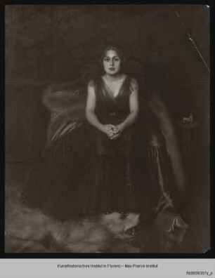 Sitzende junge Frau in Abendrobe, die Füße auf dem Kopf eines Eisbärenteppichs