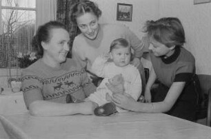 Drei Frauen und ein mit einem Teddybären spielendes Kleinkind