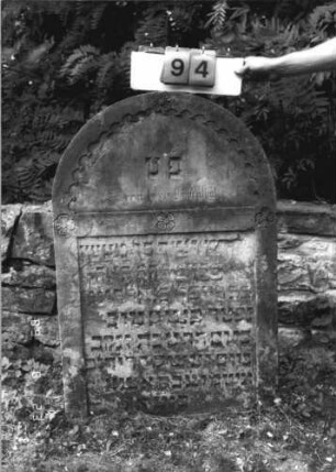 Grabstein 94 (Index: 100110777) Material: Sandstein Zustand: leicht verwittert mit einzelnen Abschieferungen, geringer Textverlust Maße HxBxT: 110x69x12 cm Beschreibung: Stele, Rundbogenabschluß mit Rundbogenfries, Schriftfelder eingetieft Symbolik: 4 Blüten: Grabstein 94