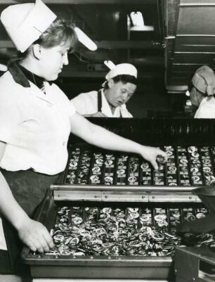 In einer Süßwarenfabrik. Arbeiterinnen nehmen Bonbons aus Formen