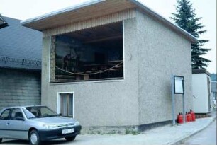 Gebäude mit Pultdach, breiter Öffnung, darin Wandmalerei und Bierzeltgarnituren
