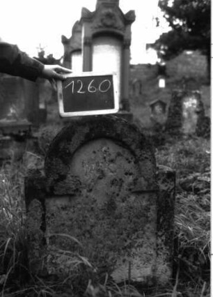 Grabstein 1260 (Index: 100104483) Material: Sandstein Zustand: stark verwittert und bewachsen, völliger Textverlust Maße HxBxT: 83x65x18 cm Beschreibung: Stele mit eingezogenem Rundbogenabschluss, Schriftfeld eingetieft mit stark eingezogenem Hufeisenbogenabschluss: Grabstein 1260