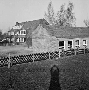 Volksschule: Schultwiete: vorn Rasen mit Jägerzaun: dahinter rechts Erweiterungsbau: links Schulhof: hinten links altes Schulgebäude: dahinter Bäume