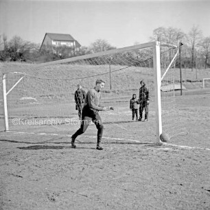 Fußballplatz: vorn Mann im Tor: dahinter Zuschauer