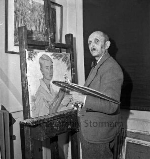 Rudolf Greve: Maler: in Atelier: vor Staffelei mit Gemälde: in Hand Pinsel und Palette