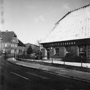 Lasbek-Dorf: Überfall: Raiffeisenbank Bad Oldesloe, Zweigstelle Lasbek: Steindamm: rechts Bankgebäude: links daneben Frau und Pkw: hinten links Bauernhäuser: Winter
