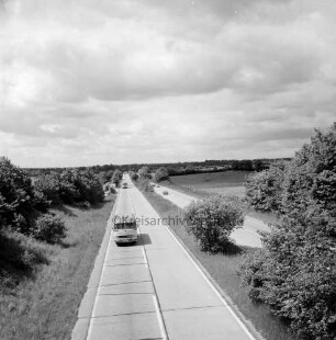 A 1: Blick von der Brücke der Bundesstraße B 75 bei Hamberge auf Autobahn: auf linker Fahrspur zwei Reisebusse, auf rechter mehrere Pkws: rechts und links Büsche und Bäume: hinten Felder und Weiden