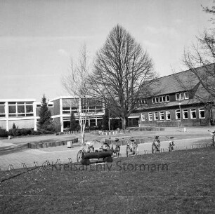 Grundschule: Hamburger Straße: ehemalige Volksschule: rechts Altbau: links Erweiterungsbauten: davor Schulhof mit Grünanlage und Baum: vorn Ständer mit Fahrrädern