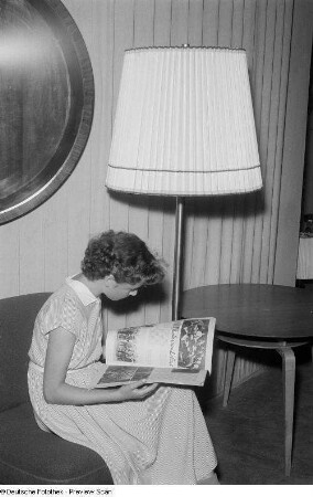 Junge Frau neben einer Stehlampe, eine Zeitung lesend