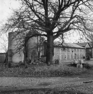 Dorfanger mit Ehrenmal: dahinter Bauerngehöft mit Silos von Heinz Burkhardt: vorn rechts Milchbock mit Milchkannen