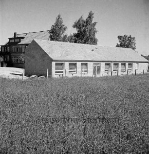Volksschule: Schultwiete: Erweiterungsbau vor Fertigstellung: Außenansicht: davor Getreidefeld: links Baumaterial: hinten links altes Schulgebäude: dahinter Bäume