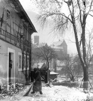 Gnandstein. Blick aus einem Gehöft mit einer alten Frau beim Schneefegen nach Südosten zur Burg Gnandstein (12.-18. Jh.)